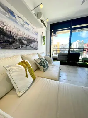 a living room with a white couch and a large window at Apartemento piscina centro calella 3 min playa in Calella