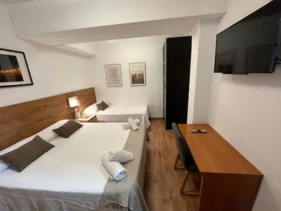 a room with two beds and a desk and a television at Hostal Alogar in Barcelona
