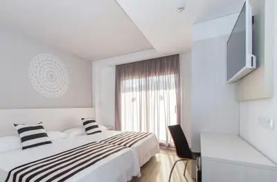 a white bedroom with a bed and a window at Hotel Oasis Park Splash in Calella