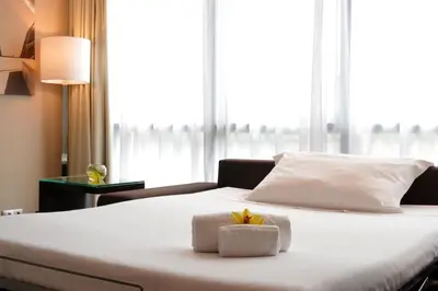 a white bed with two towels and a flower on it at Pestana Arena Barcelona in Barcelona