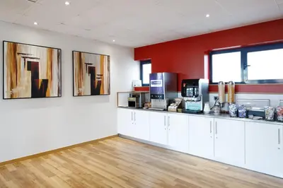 a kitchen with white cabinets and a red wall at Travelodge Barcelona Fira in Hospitalet de Llobregat