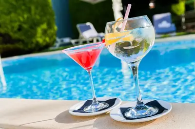 two martini glasses sitting on a table next to a pool at PARK SEDO Aparthotel in Rubí