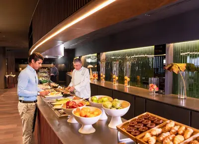two chefs preparing food at a buffet in a restaurant at BAH Barcelona Airport Hotel in El Prat de Llobregat
