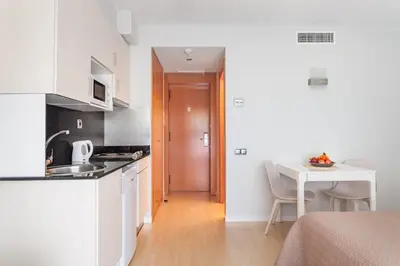 a kitchen with white cabinets and a table and a table at Apartamentos Royal Marina Gardens in Castelldefels
