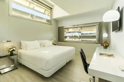 a white bedroom with a white bed and a table at NH Collection Barcelona Constanza in Barcelona