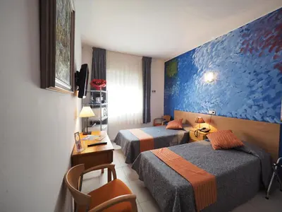 a hotel room with two beds and a desk at Hotel Montserrat in Sitges
