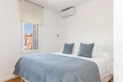 a white bedroom with a bed with blue sheets and a window at Idyllic apartment in BCN beach in Barcelona