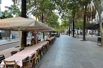 a row of tables and chairs with umbrellas on a street at NEW! Amazing 2 bedroom apartment in Rambla del Poblenou in Barcelona