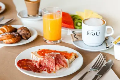 a table with plates of breakfast food and a cup of orange juice at Checkin Montserrat in Collbató