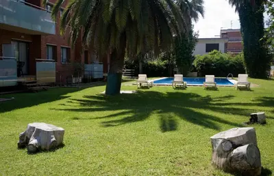 a park with a palm tree and chairs and a pool at SG Costa BCN Apartments in Castelldefels