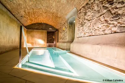 a swimming pool in a building with a stone wall at Balneari Termes Victòria in Caldes de Montbui