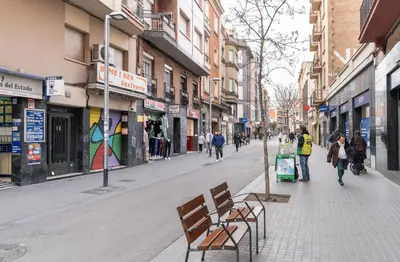 a street with two benches and people walking down the street at Caliu Apartments Barcelona - Camp Nou in Hospitalet de Llobregat