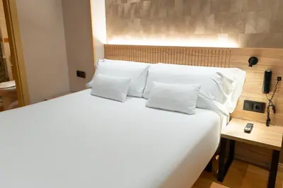 a large bed with white pillows and a phone at Petit Palace Eixample in Barcelona