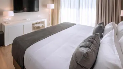 a bedroom with a large white bed with a couch at Hotel Playafels in Castelldefels