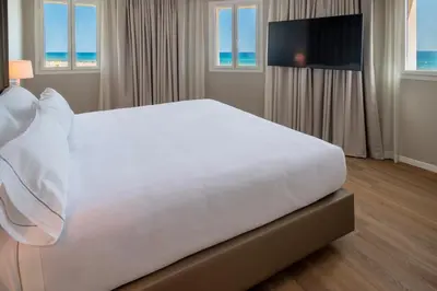 a large white bed in a hotel room with a television at Hotel Playafels in Castelldefels
