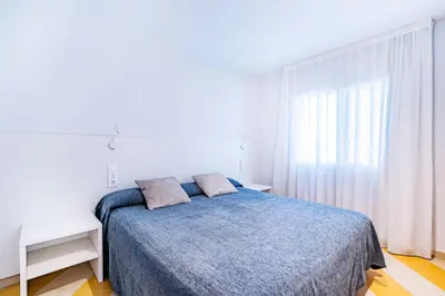 a white bedroom with a blue bed and a window at Apartamentos Sunway Amapola in Sitges