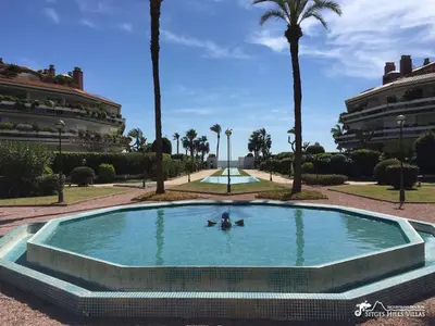 a pool in a park with palm trees and a building at Apt Parc Del Mar in Sitges very near Beach in Sitges