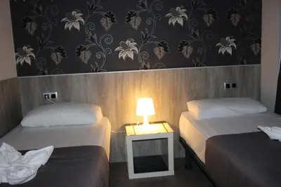 a room with two beds and a table with a lamp at BCN Condal Hostal in Barcelona
