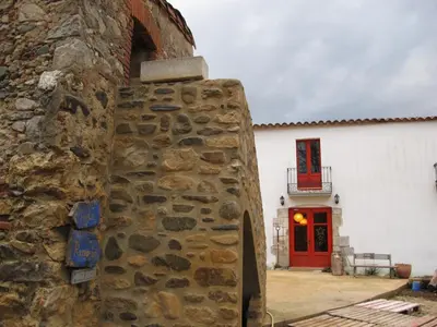 a building with a stone wall and a red door at Mas Can Puig de Fuirosos ONLY ADULTS in La Batlloria