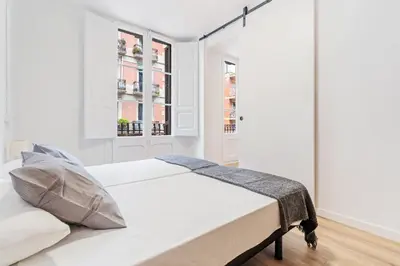 a white bedroom with a bed and two windows at AB Nou de la Rambla in Barcelona