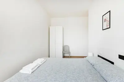 a white bedroom with a bed and a chair at The Collection Barcelona - Comfortable 3BD in Poblenou next to the beach only for Families! in Barcelona