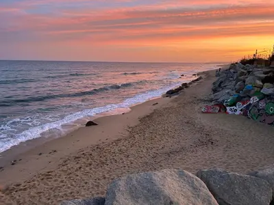 a beach with rocks and the ocean at sunset at Vilamarlux VII in Vilassar de Mar